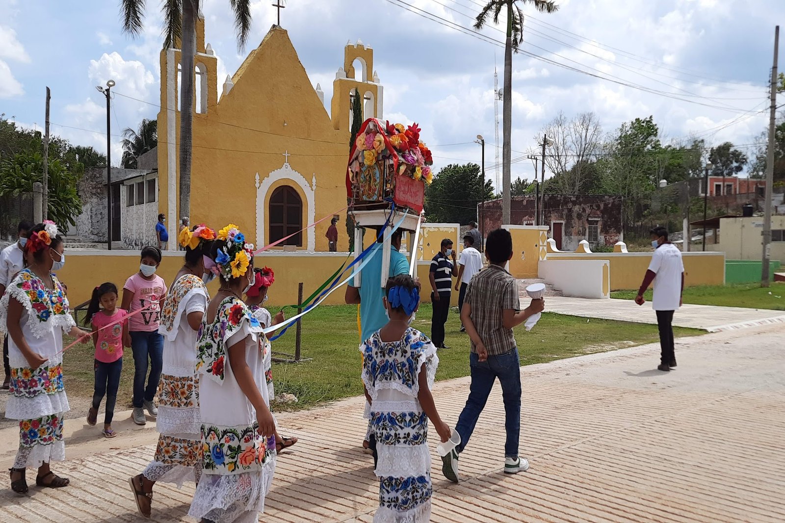 Procesión comunitaria con mujeres en huipil frente a iglesia